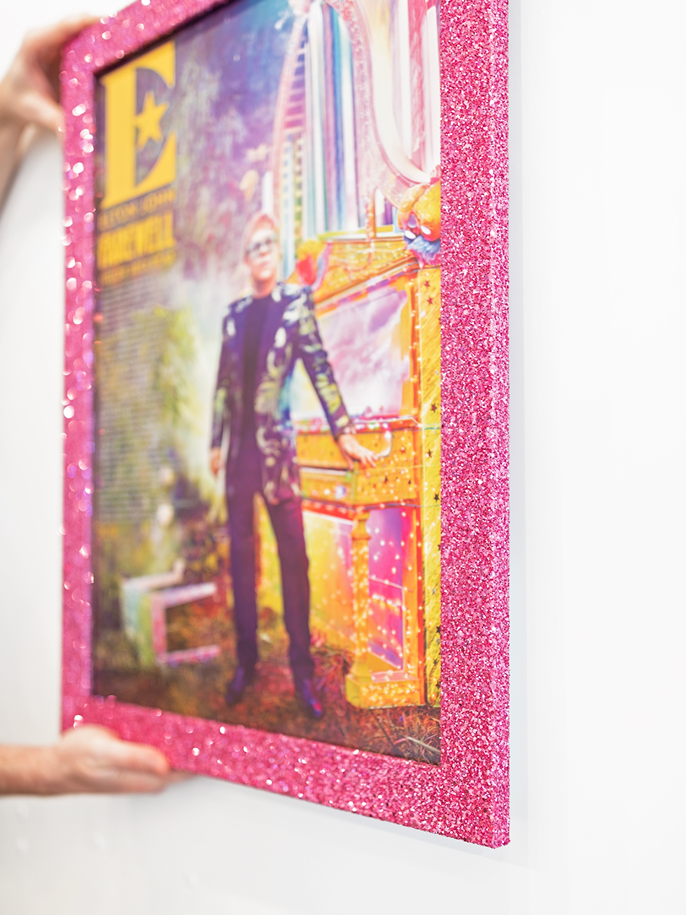 Details of a pink glitter frame on an Elton John Farewell Yellow Brick Road concert poster.