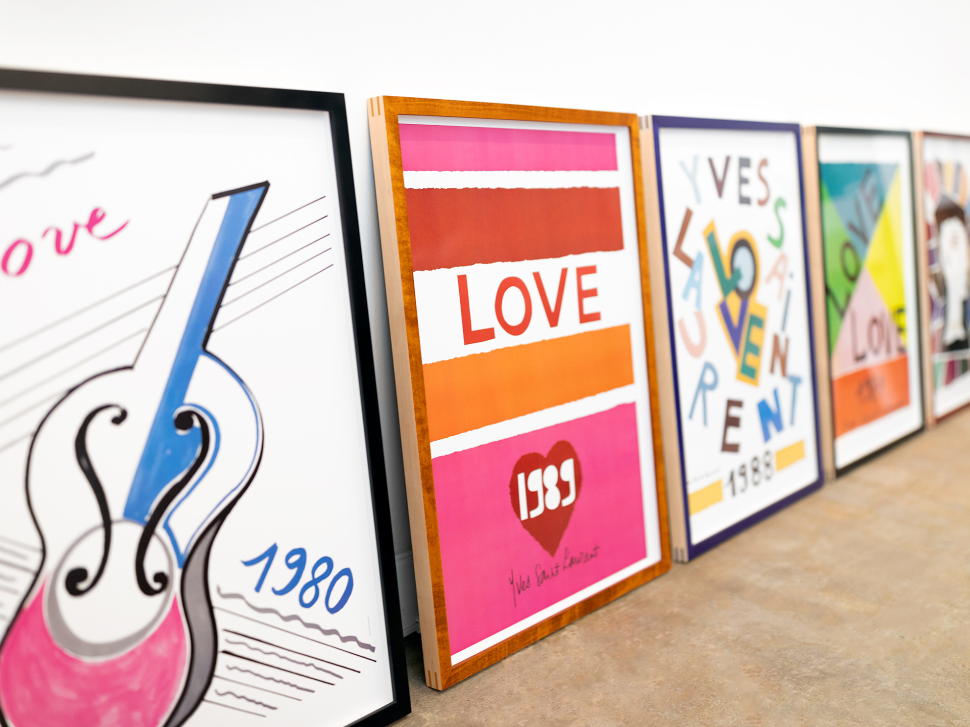 Side view of a series of vintage 1980's Yves Saint Laurent posters custom framed in colorful stained maple wood frames.